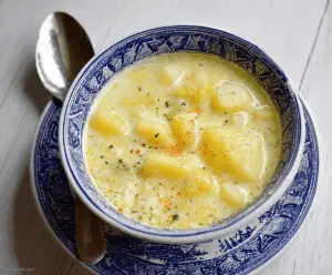 A bowl of homemade Grandma's Potato Soup garnished with fresh herbs, served with crusty bread on a rustic wooden table.