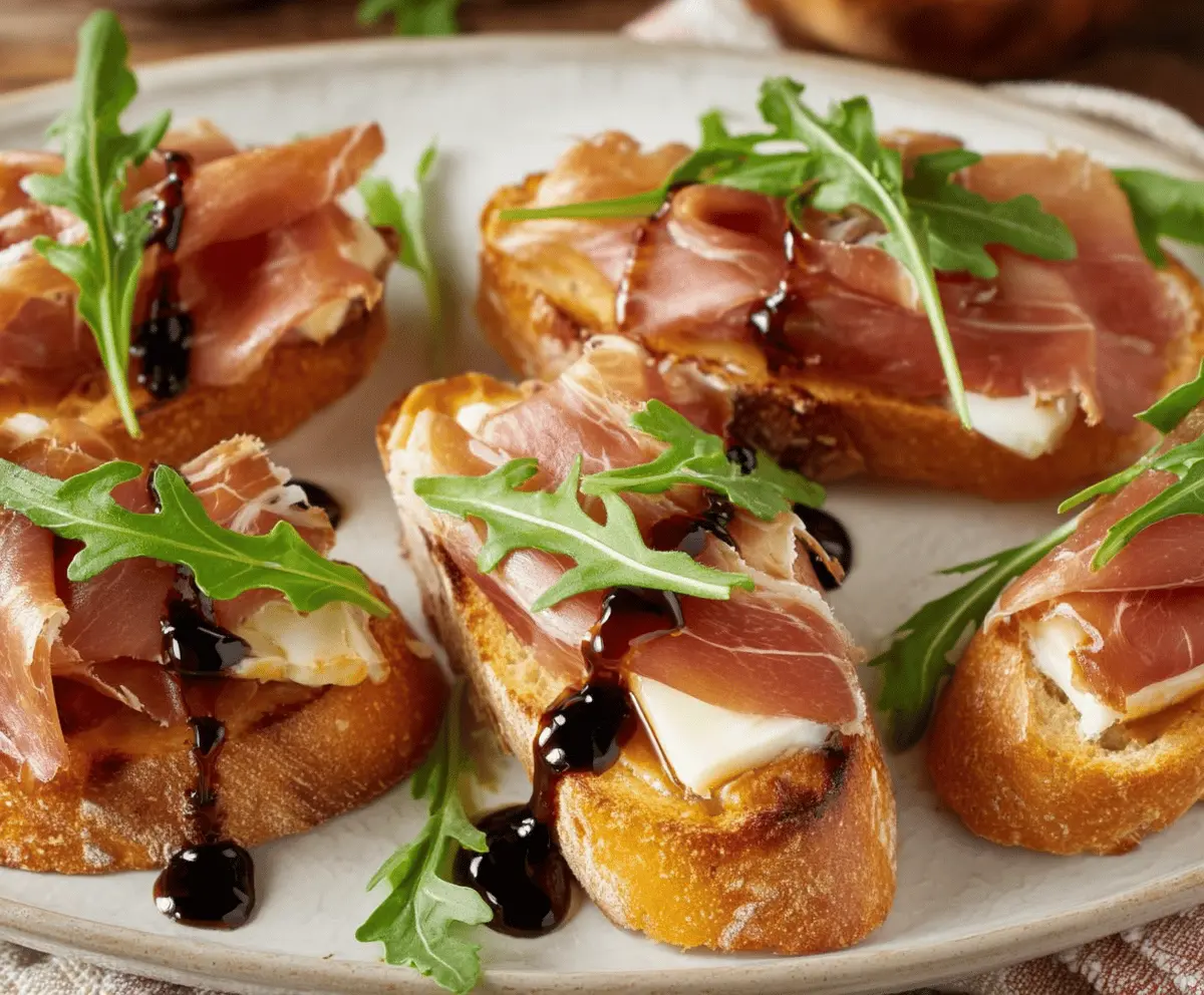 Brie and prosciutto crostini served on a rustic platter, garnished with fresh herbs.