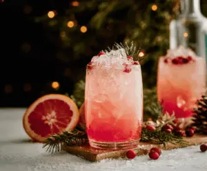 Festive Christmas Paloma cocktail garnished with a slice of lime and a cherry on a holiday-themed background.