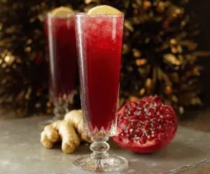 Fizzy Pomegranate Ginger Sparkler in a clear glass with fresh pomegranate seeds and ginger slices