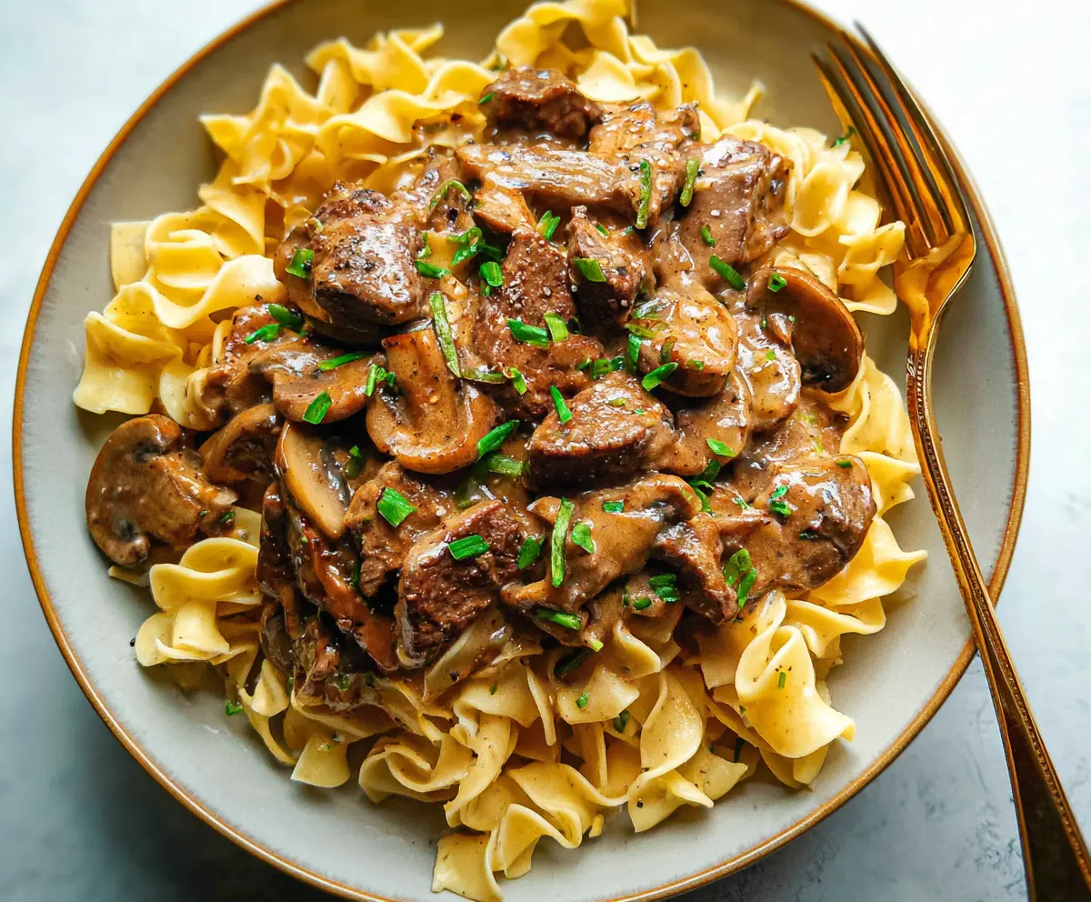 Creamy beef stroganoff served over tender noodles, garnished with fresh herbs.