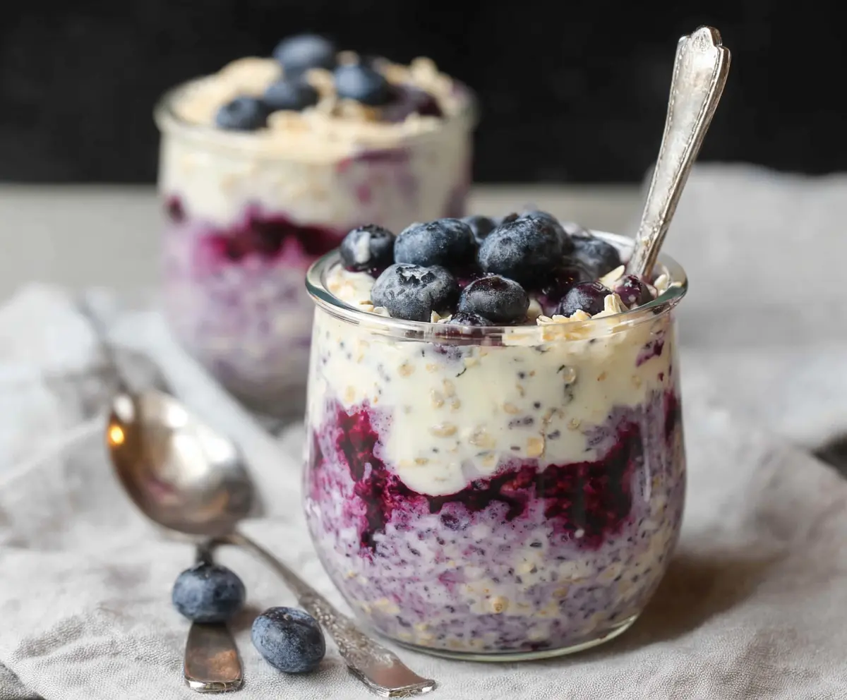 Creamy blueberry cheesecake overnight oats in a jar with fresh blueberries on top.