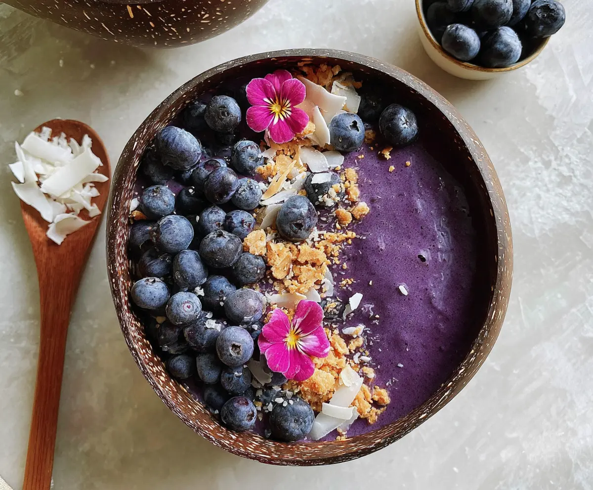 Colorful blueberry smoothie bowl topped with fresh blueberries and granola on a white plate.