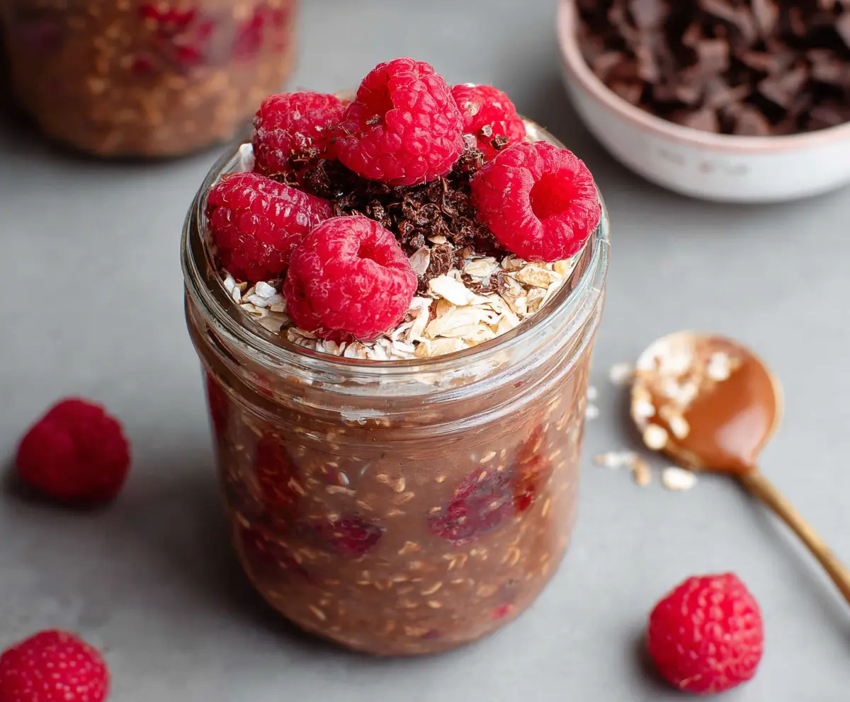 Creamy chocolate raspberry overnight oats in a glass jar with fresh raspberries on top
