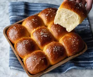 Golden baked sourdough brioche bread rolls stacked on a wooden surface, showcasing their soft, fluffy texture and shiny crust.