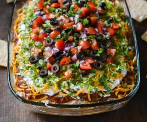Delicious 7 Layer Bean Dip with fresh vegetables, cheese, and salsa served in a glass bowl.
