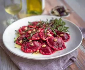 Beautiful beet heart ravioli on a plate, showcasing vibrant red pasta with fresh basil garnish.