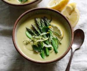 Creamy tahini and lemon asparagus soup served in a bowl with fresh herbs and lemon slices.