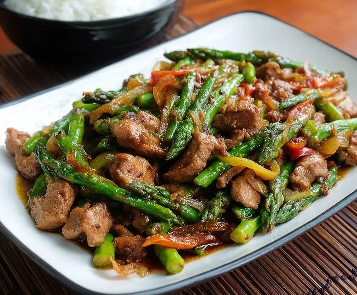 Delicious pork and asparagus stir fry served on a plate with colorful vegetables.