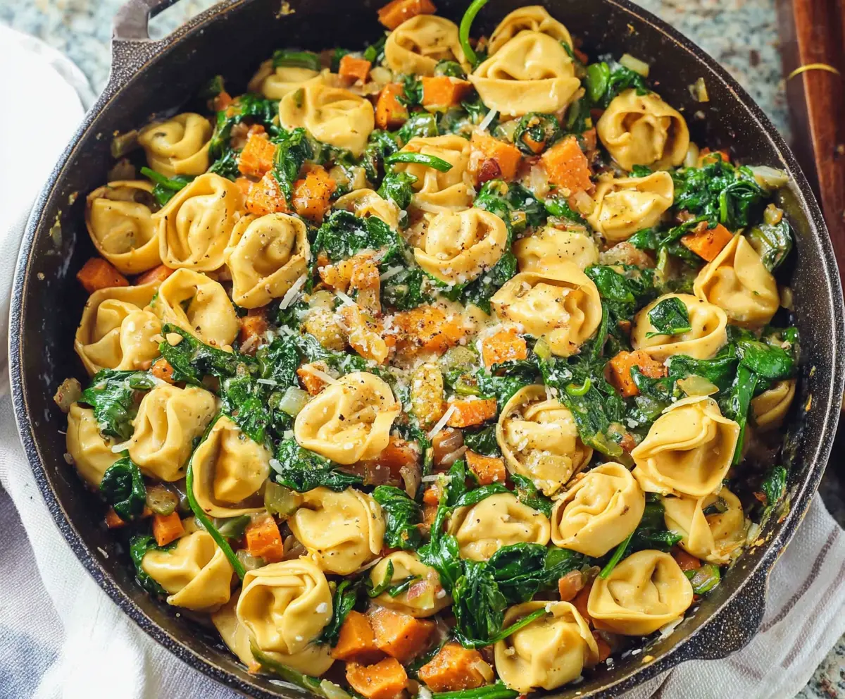 Delicious skillet tortellini with sweet potato and fresh spinach on a white plate.