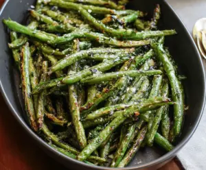 Delicious roasted green beans garnished with herbs on a white plate.